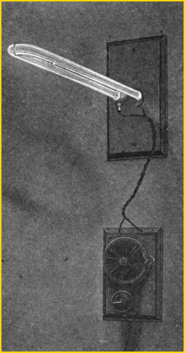 A historic photograph of Peter Cooper Hewitt's first mercury vapor lamp from 1903. The image shows a long, horizontal glass tube with electrodes, positioned above a circular electrical ballast. This invention was the direct predecessor of the modern fluorescent light.