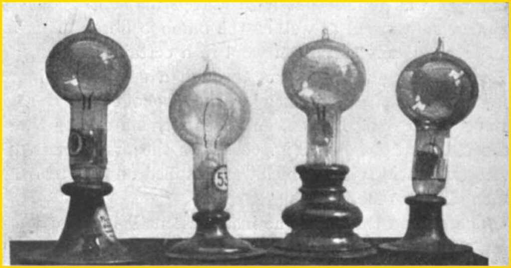 Close-up photograph of two early Thomas Edison incandescent light bulbs from 1879, showcasing the distinctive horseshoe-shaped paper filaments inside the glass globes.